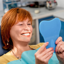Woman in the patient’s chair smiling in small mirror