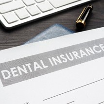 Closeup of dental insurance paperwork with a laptop, money, and pens in the background 