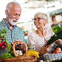 Senior couple smiling while filling basket with fresh produce
