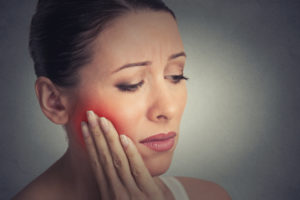 Woman with facial swelling holding hand to jaw 